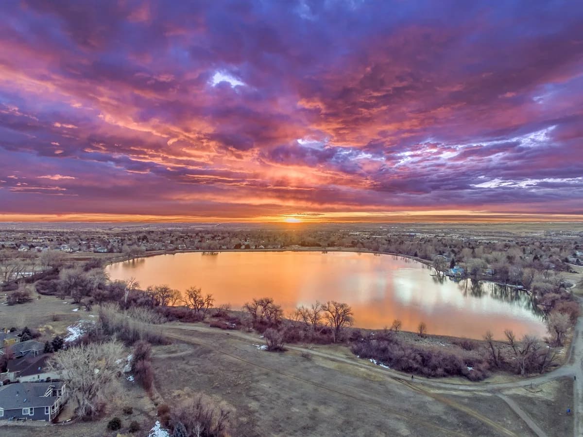 A dramatic sunset over a lake, captured in an impressionistic photographic style with vibrant Copperfield and Coral Tree hues.